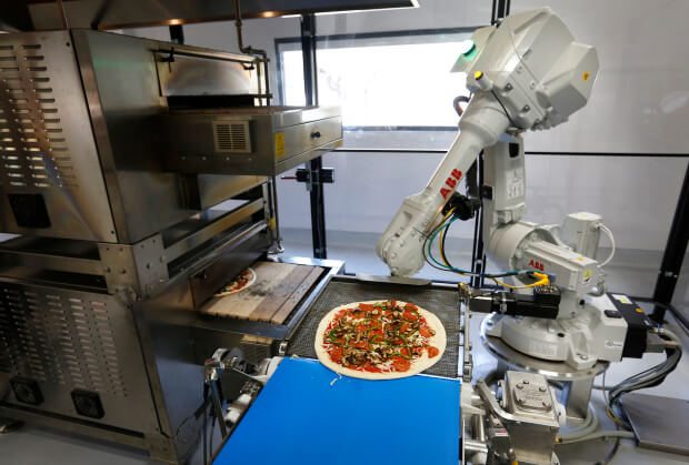 A robot places pizzas into an oven as it comes off a conveyer belt at Zume Pizza in Mountain View, Calif., Wednesday, Aug. 24, 2016. Zume Pizza uses robots to make customers' pizza, hoping to reduce labor costs and therefore make pizza a more profitable venture. One robot spreads the sauce on the uncooked pies, then humans add toppings, and another robot pops it in the oven. They are also hoping to use delivery trucks with smart ovens to cook pies en route to customers. (Patrick Tehan/Bay Area News Group)